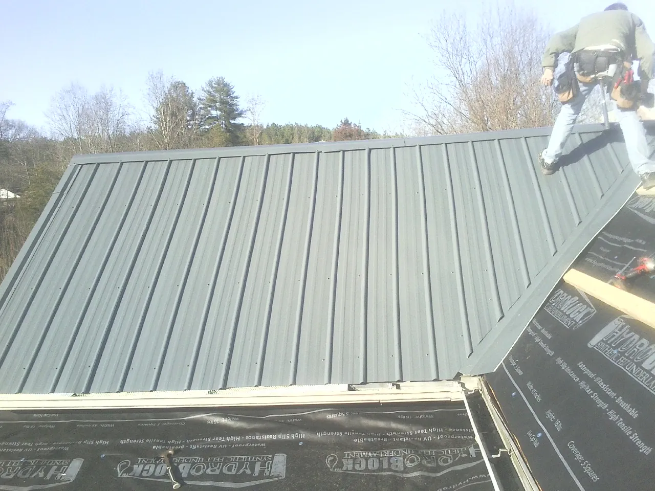 Crew installing dark green standing seam panels over synthetic underlayment in Tustin