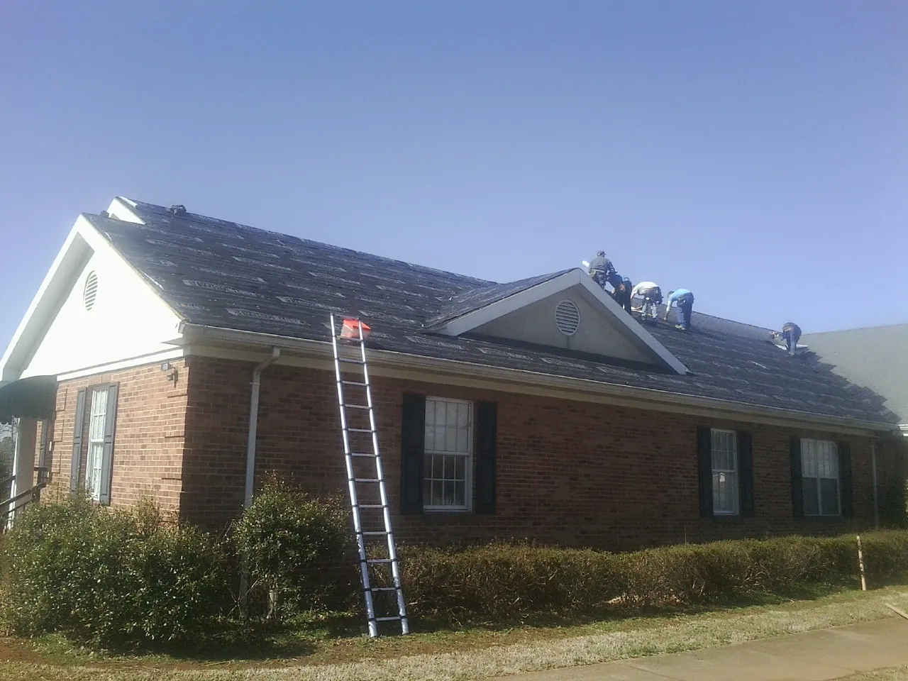 Crew tearing shingles off a brick ranch roof with a ladder set — Metal Roof Repair work by our crew in Tustin