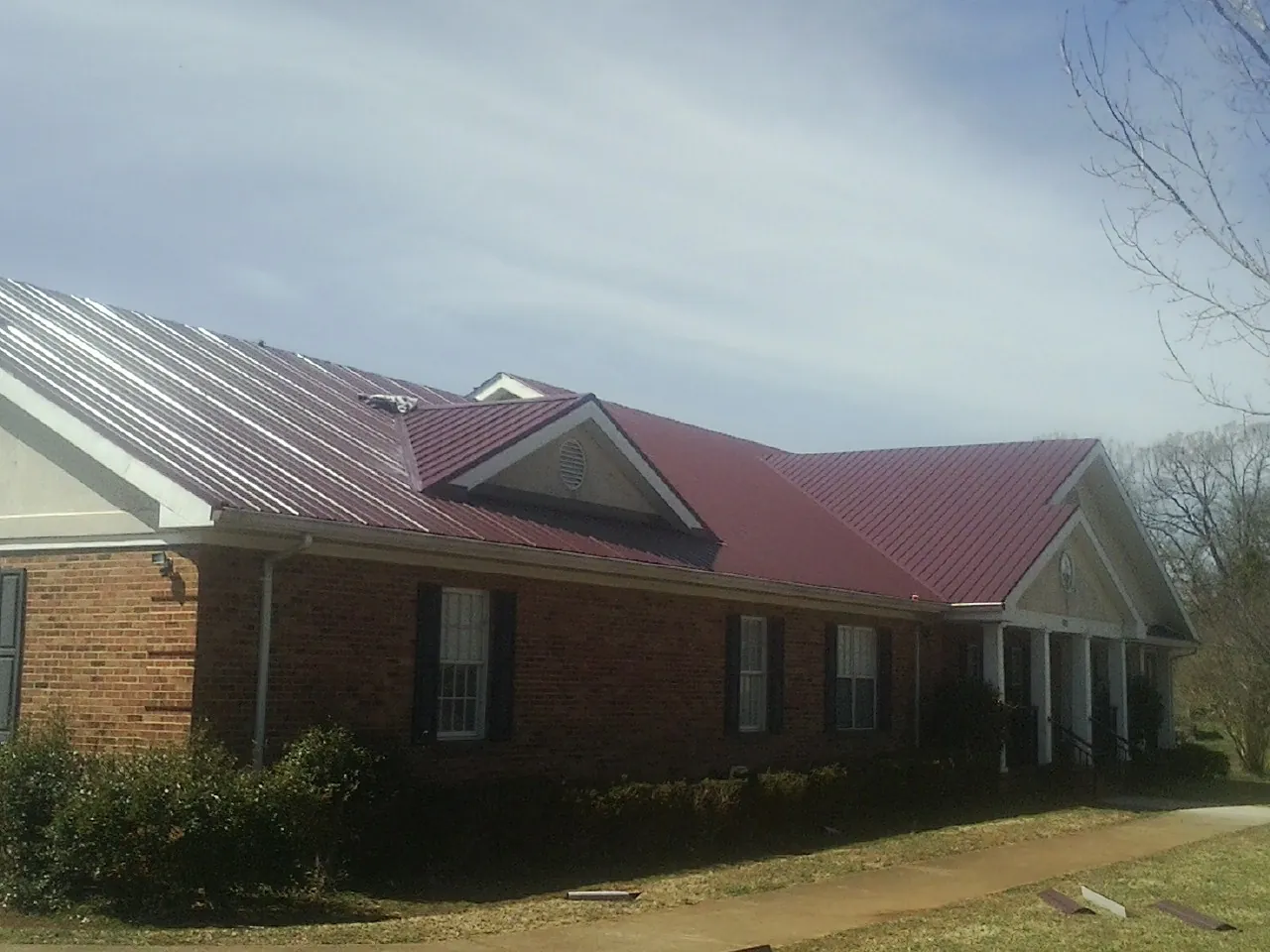 Red metal roof with gabled entries on a long brick building, from a Hail Damage Roof Repair job in Tustin