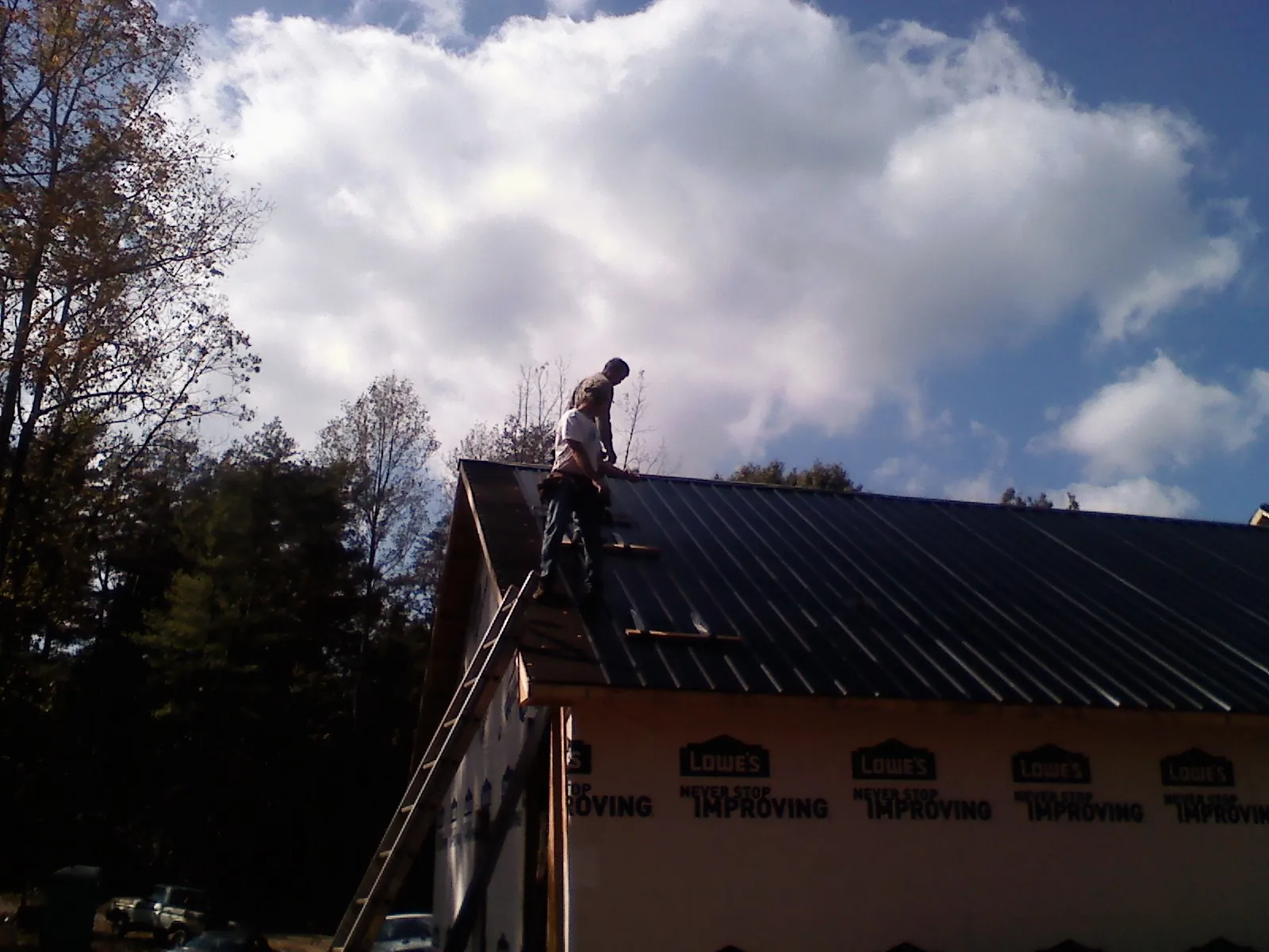 Roofer fastening dark metal panels high against a cloudy sky, from a Roof Inspection job in Tustin