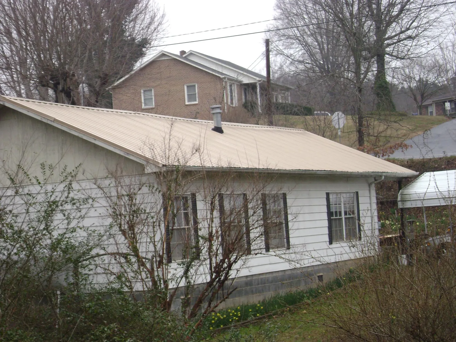 Tan metal roof on a white sided house set into a hillside — Commercial Roofing by Roofing Brothers in Tustin