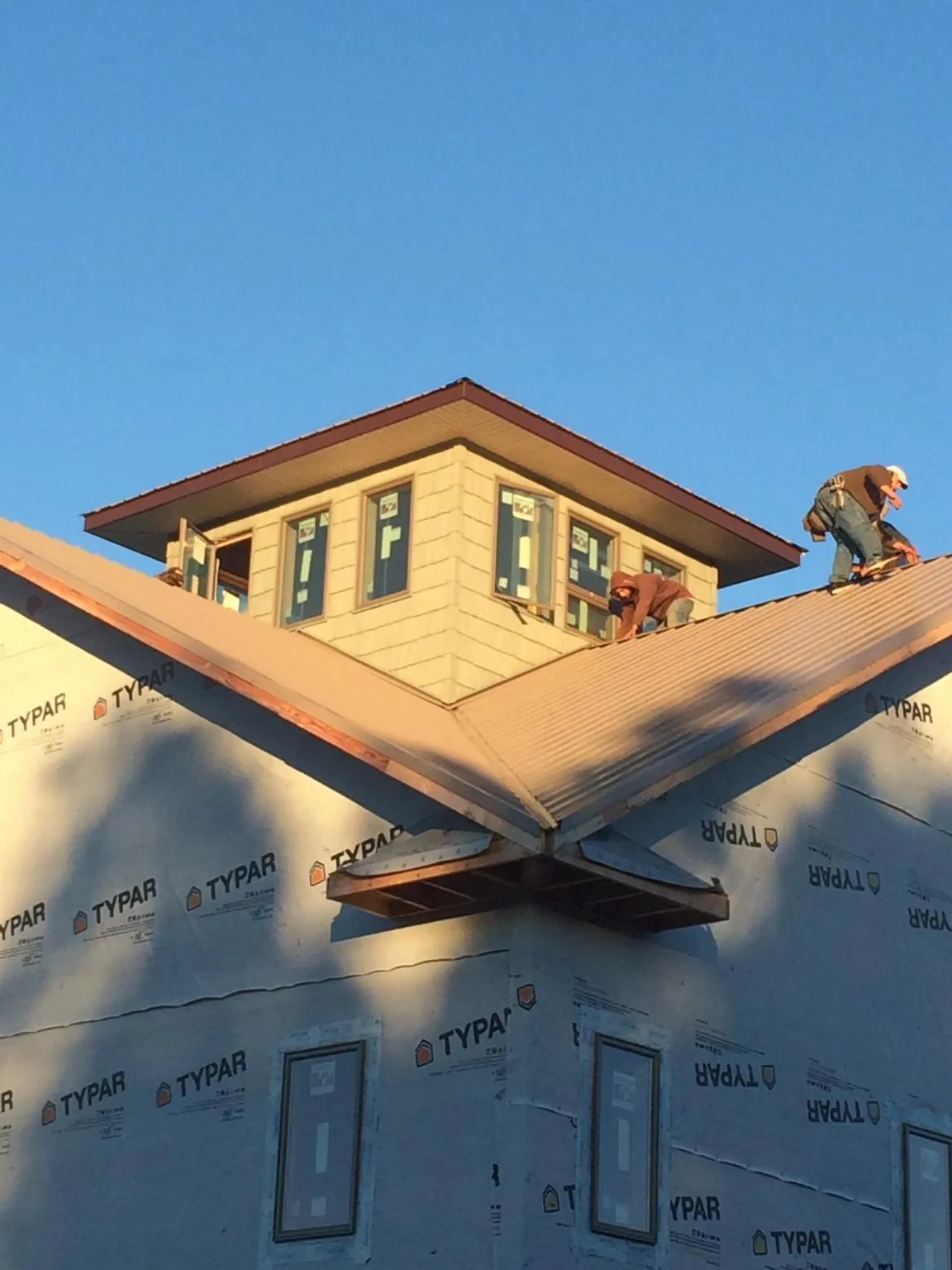 Roofers working around a rooftop cupola on a new metal roof at sunset — Roof Waterproofing in Tustin by Roofing Brothers